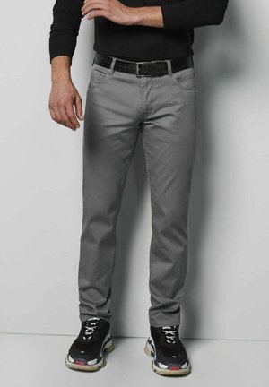 Grijze slim-fit broek met een platte voorkant, vier zakken en een zwarte gestructureerde riem. Draagt zwart sneakers met witte accenten en veters.