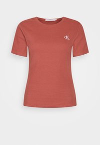 Krátký rukáv, žebrované tričko v terakotové barvě s kulatým výstřihem. Má malé bílé vyšívané logo "CK" na hrudi.