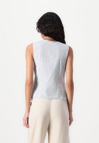 Haut sans manches en bleu clair avec des rayures verticales blanches, fabriqué à partir d'un tissu doux. L'ourlet est légèrement arrondi ; le dos a une encolure ronde.