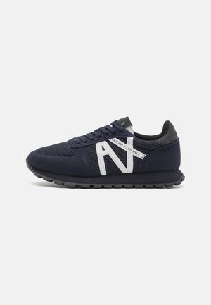 Sneaker bleu marine en matériau mesh et daim, présentant un grand logo "A" blanc, une semelle texturée et des accents noirs sur le talon et la languette.