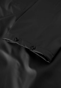 Tissu noir imperméable avec une texture lisse, présentant un bord replié et deux boutons-pression noirs pour une fermeture sécurisée.