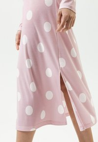 Rosa Kleid mit weißen Polka-Dots, langen Ärmeln, seitlichem Schlitz und glatter Stoffstruktur. Verfügt über einen runden Ausschnitt und eine legere Passform.