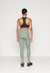 Sujeción deportiva negra de tirantes en forma de racerback combinada con leggings de cintura alta en verde claro y zapatillas deportivas negras; tejido suave y ajustado con costuras mínimas.