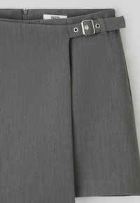Jupe plissée grise avec une ceinture et une boucle en argent, fabriquée en tissu lisse. Comprend une fermeture éclair dissimulée et une finition soignée et ajustée.