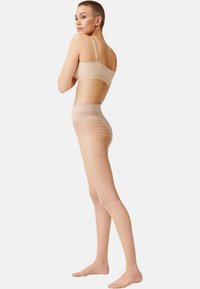 Soutien-gorge nude sans couture et collants taille haute avec des sections transparentes. Les collants présentent des rayures horizontales et une texture lisse.