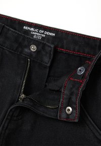 Vaqueros de mezclilla negros con costuras rojas, cremallera parcialmente desabrochada, cierre de botón y etiqueta que dice "Republic of Denim Carpenter" tamaño 110 cm, 4-5 años.