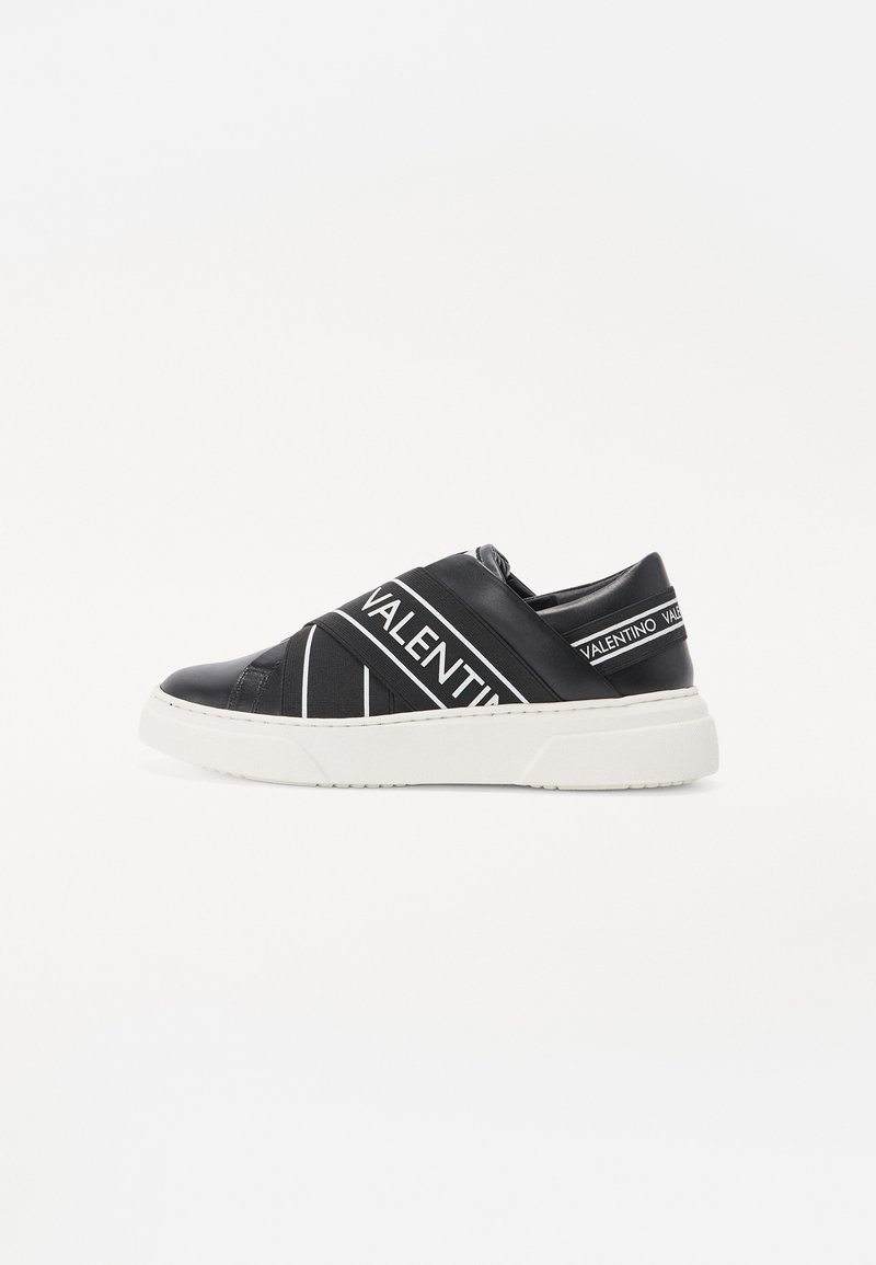 Baskets noires à enfiler avec des sangles décoratives blanches portant le texte "VALENTINO". Semelle en caoutchouc blanche, matériau supérieur lisse et design à rayures diagonales.