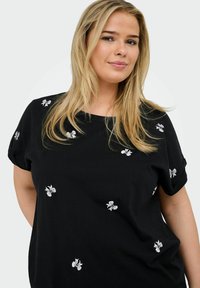 Svart kortärmad topp med rund halsringning, prydd med vit blommig broderi spritt över tyget. Mjuk bomullsmaterial, avslappnad passform.