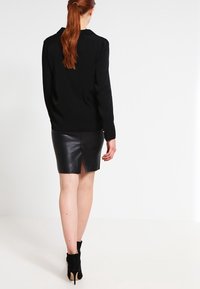 Maglione nero a maglia con scollatura rotonda, abbinato a una mini gonna in pelle nera aderente con uno spacco sul retro e stivaletti neri alla caviglia.