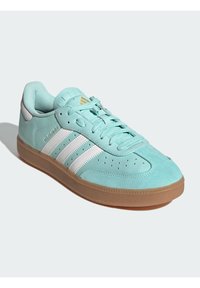 Jasnoniebieskie zamszowe sneakersy z białymi paskami, z gumową podeszwą, okrągłym noskiem i perforowanymi detalami. Złote akcenty logo.