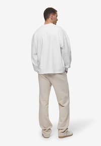 Sudadera blanca de gran tamaño con hombros caídos, combinada con pantalones de chándal beiges y zapatillas blancas. Textura suave, corte relajado.