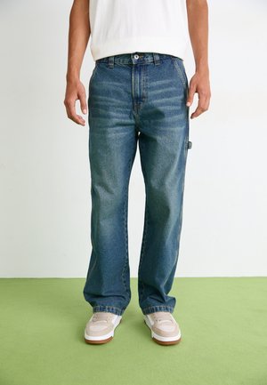 Light blue denim jeans with a straight-leg cut, featuring a classic five-pocket design and contrast stitching. Worn with beige sneakers.