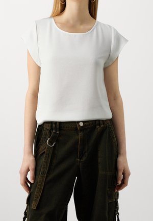 Blouse blanche à manches courtes avec un col rond, fabriquée à partir d'un tissu texturé, associée à un pantalon cargo vert foncé avec des poches latérales.