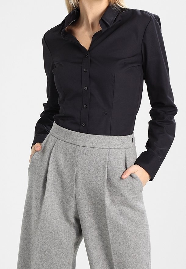 Chemise noire à boutons avec manches longues et col, associée à un pantalon en laine gris taille haute présentant des poches latérales et des détails plissés.