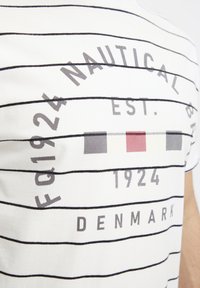 Baltos dryžuotos marškinėliai, turintys tamsiai mėlynus horizontalius dryžius, grafinius užrašus pilka ir raudona spalva, bei švelnų medvilnės paviršių. Dizainas apima jūrinę tematiką.