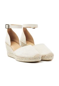 Beige suede espadrilles with wedge heels, ankle straps, and woven jute detailing along the sole. Smooth texture and minimalist design.