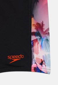 Calções de natação pretos com uma estampa abstrata vibrante de palmeiras. Logótipo "Speedo" em laranja brilhante perto da costura. Textura de tecido suave.