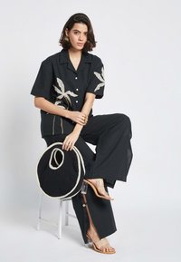 Maglietta nera a maniche corte con ricamo bianco a foglia, pantaloni neri a gamba larga, sandali con tacco trasparente e borsa rotonda in rete nera.