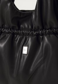 Zwarte faux leren schoudertas met een verzameld ontwerp, voorzien van een zilveren metalen logoplaat, een soepele textuur en een afgeronde opening aan de bovenkant.