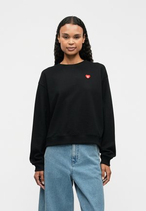 Czarna bluza wykonana z bawełny, z okrągłym dekoltem i obniżonymi ramionami. Na piersiach znajduje się małe czerwone serce.
