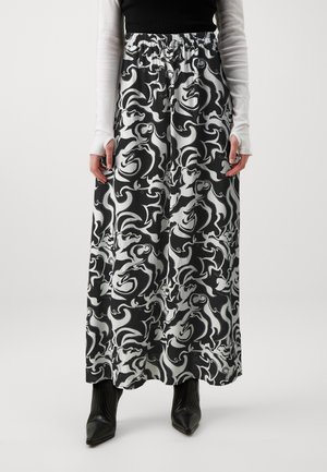 Personne portant une longue jupe à motif abstrait noir et blanc, des bottes noires pointues, un haut noir et des gants blancs à manches longues.