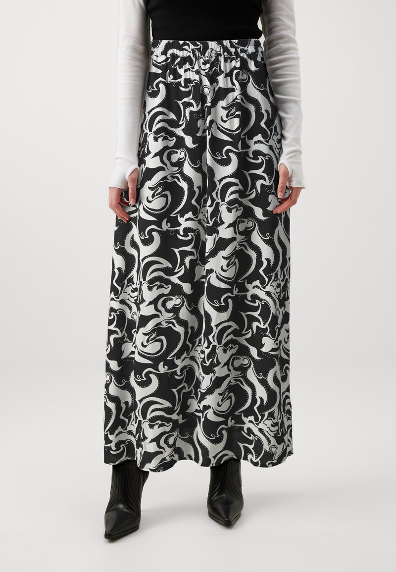 Personne portant une longue jupe à motif abstrait noir et blanc, des bottes noires pointues, un haut noir et des gants blancs à manches longues.