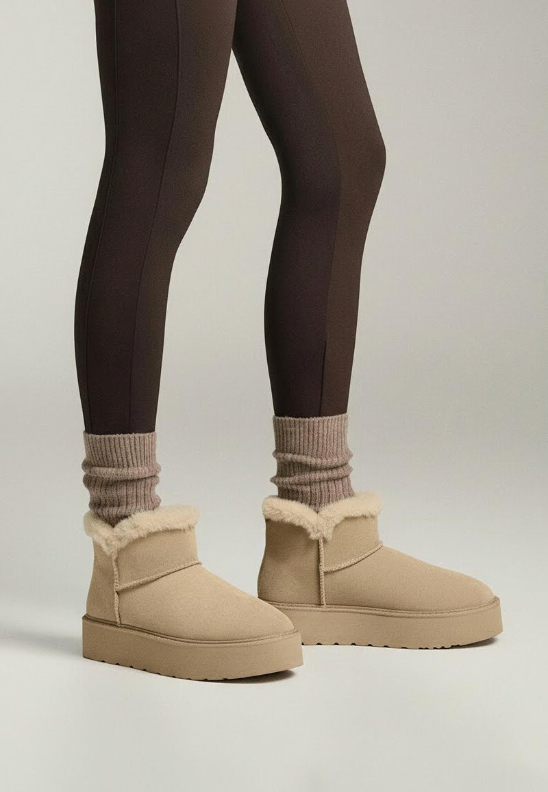 Beige ankelkängor med fuskpäls, gjorda av mjukt material, med grov sula och minimalistisk design. Bärs med ribbade strumpor.