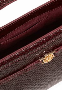 Burgundy, snake-print handbag with a glossy texture, gold hardware clasp, and multiple interior compartments for organization.