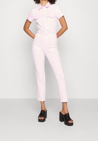 Rosa denimoverall med korta ärmar, två bröstfickor, en linning i midjan och raka byxor. Bärs med kraftiga svarta platåsandaler.