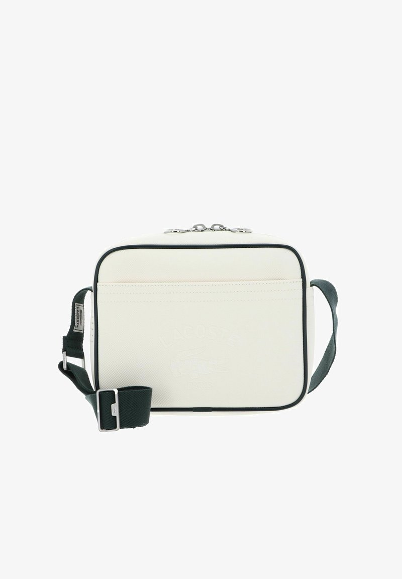 Sac bandoulière rectangulaire blanc avec une bordure noire, une sangle réglable vert foncé et un logo Lacoste embossé à l'avant.