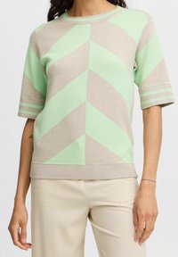 Pull en tricot avec un motif en chevron vert menthe et beige, manches courtes et accents rayés aux poignets.