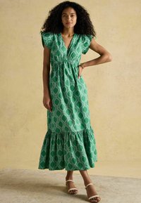 Grün gemustertes Maxikleid mit rüschengesäumtem Saum und kurzen Ärmeln. Hat einen V-Ausschnitt und einen elastischen Taillengürtel für eine bequeme Passform.