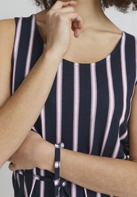 Tummansininen ilmanhiha, jossa on pystysuorat vaaleanpunaiset ja valkoiset raidat, pyöreä kaula-auko, ja nauhadetail vyötäröllä, valmistettu pehmeästä ja joustavasta materiaalista.