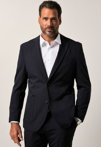 Giacca da abito blu navy con due bottoni, rever a punta e due tasche frontali. Abbinata a una camicia bianca sotto, dalla texture liscia.
