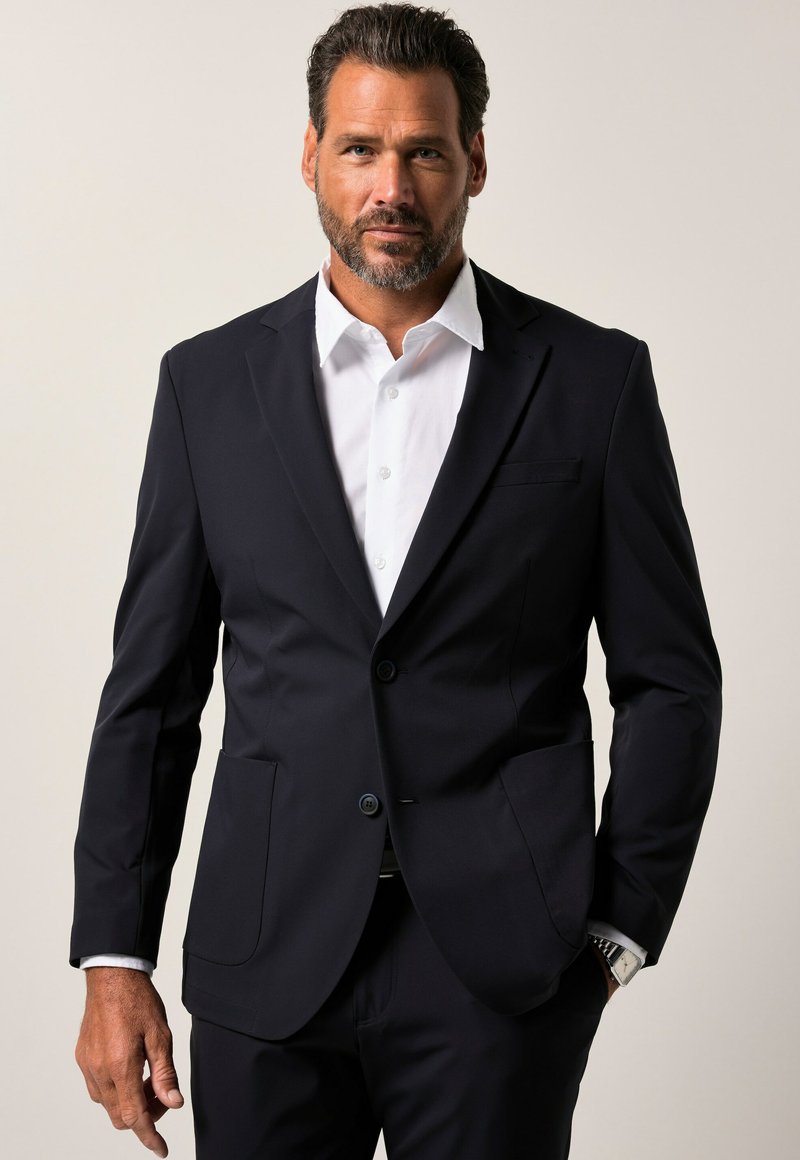 Giacca da abito blu navy con due bottoni, rever a punta e due tasche frontali. Abbinata a una camicia bianca sotto, dalla texture liscia.