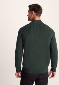 Green ribbed sweater with a high collar and raglan sleeves, featuring textured knit fabric and a fitted waistband.
