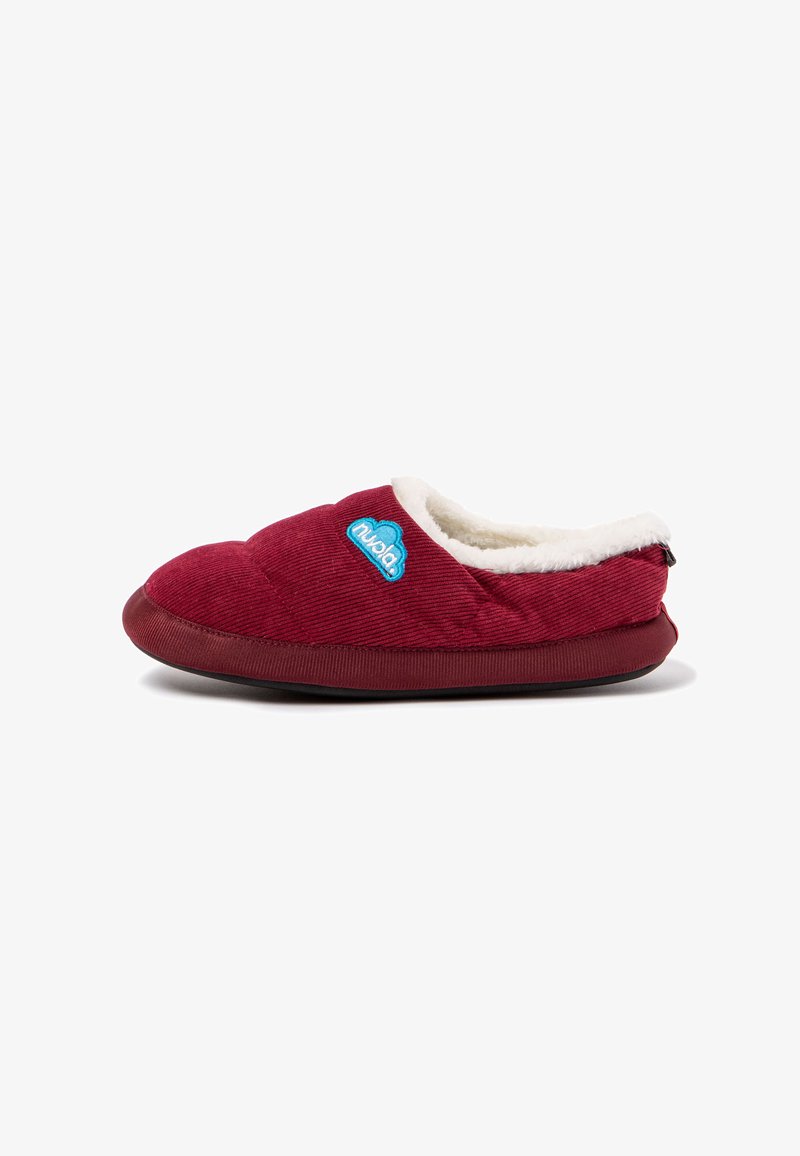Zapatilla de corduroy roja con un suave forro blanco, textura acolchada y un logo azul. Diseño de tipo slip-on con una suela de goma flexible.