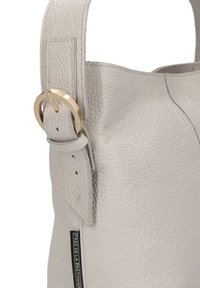 Lichtgrijze leren tas met een textuur en een gouden hardware accent. Heeft een platte schouderband met een gespdetail.