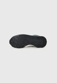 Suela de goma negra con un patrón de tracción en zigzag, con material superior verde y mínimos acentos blancos. Textura suave en todo.