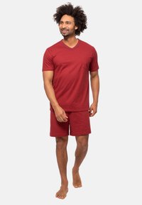 Punainen puuvillainen t-paita, jossa on V-pääntie ja tasku, yhdistettynä vastaaviin punaisiin shortseihin. Kangas näyttää pehmeältä ja sileältä.