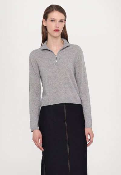 Γκρι ζακέτα με φερμουάρ και μακριά μανίκια, φτιαγμένη από μαλακό υλικό, με ριγωτή βάση και γιακά. Συνδυάζεται με μια σκούρα φούστα.