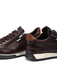 Zapatillas de cuero marrón con acabado texturizado, con cordones en la parte delantera, cremalleras laterales y un tacón más claro que contrasta. Suela de goma para mejor agarre.