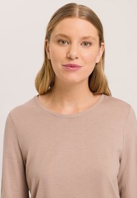 Lange mouw top van zacht beige stof met een ronde halslijn. Gladde textuur en een aansluitend ontwerp. Geen patronen of zichtbare hardwaredetails.