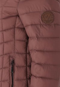 Puffjakke i en dæmpet mauve farve, med et quiltet design, en lynlåslomme og et rundt logo patch på ærmet.