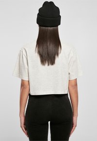 Krótkie beżowe t-shirt z krótkimi rękawami, zestawiony z czarnymi ryflowanymi legginsami i czarną wełnianą czapką. Widok z tyłu.