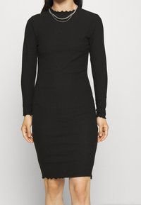 Černé žebrované šaty s dlouhým rukávem, tvarující siluetu, se zvlněným výstřihem a lemem, vyrobené z hladkého a pružného materiálu.