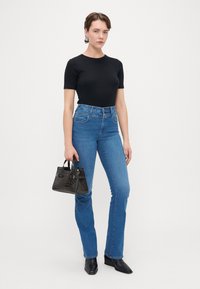 Musta lyhythihainen paita, korkeavyötäröiset siniset farkut, slim fit. Kantaa pientä mustaa krokotiilinasuista käsilaukkua. Mustat teräväkärkiset nilkkurit.