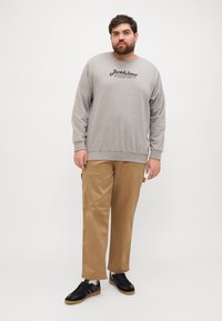 Sweatshirt gris à manches longues et col rond, assorti avec un pantalon beige clair. Des baskets noires complètent la tenue.