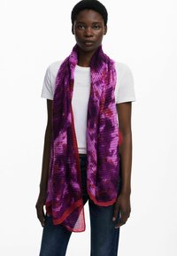 Écharpe à motifs violets et rouges en tissu texturé, présentant un design rayé et une forme fluide, drapée autour du cou du modèle.