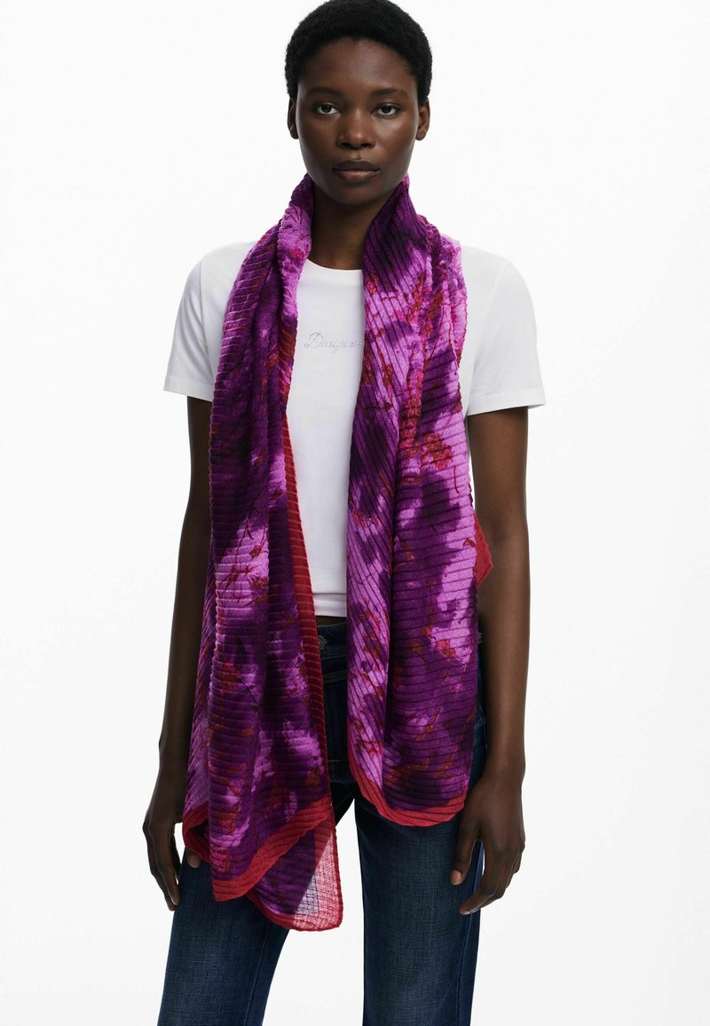 Écharpe à motifs violets et rouges en tissu texturé, présentant un design rayé et une forme fluide, drapée autour du cou du modèle.